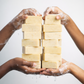 Three hands holding a stack of soap bars against a white background