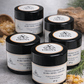 Jars of Ultra Viridis cold weather body butter on a gray surface with natural elements.