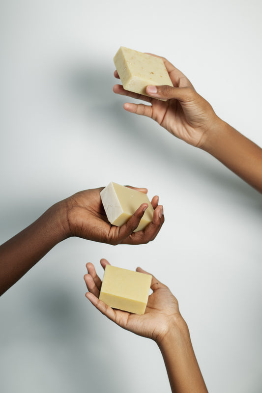 Three hands holding bars of soap against a light gray background
