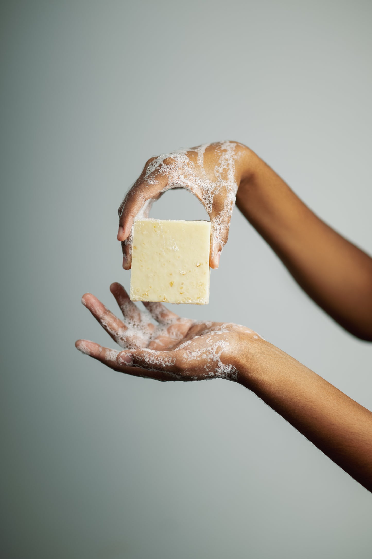Hands holding a bar of soap against a gray background