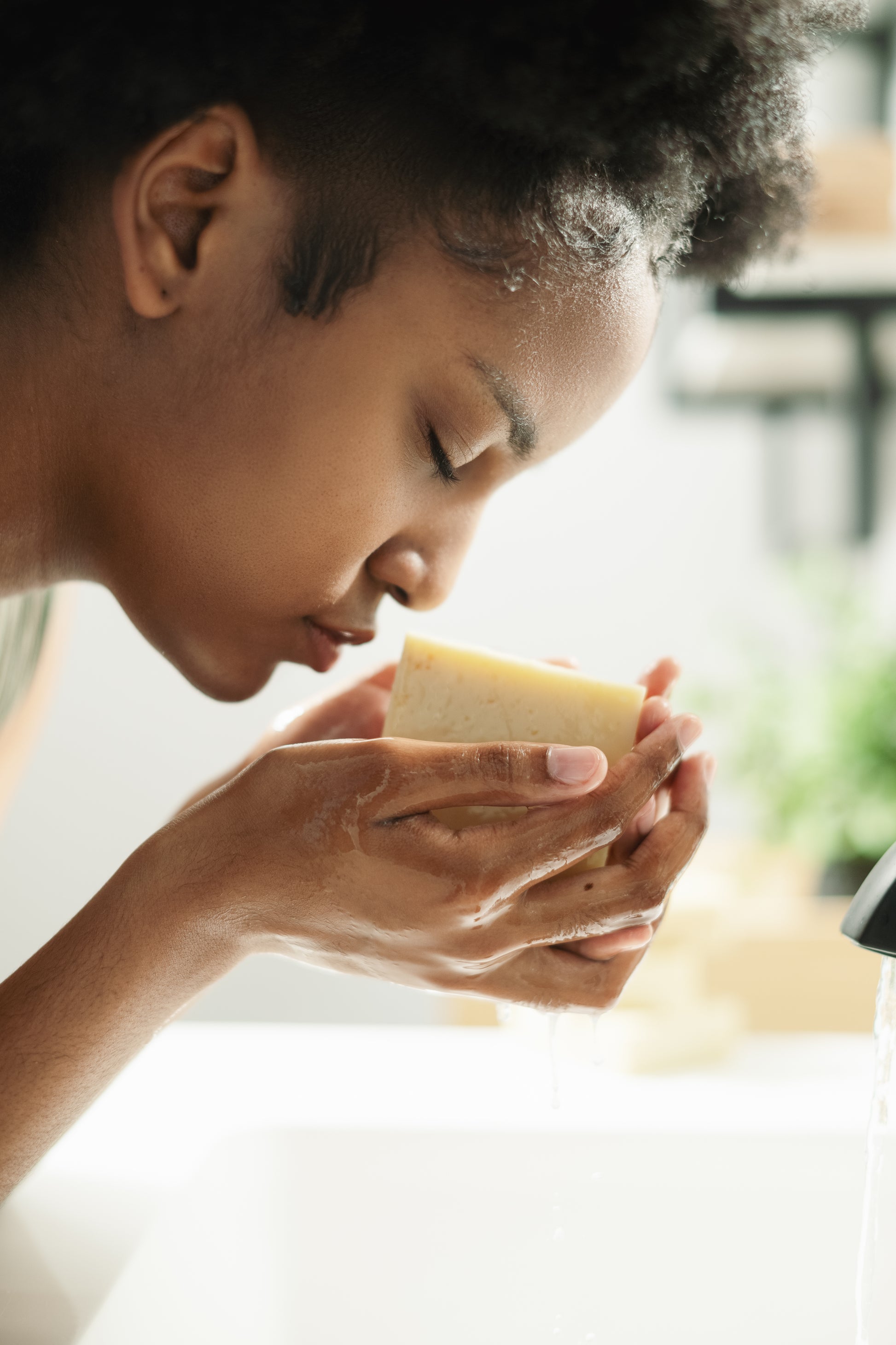 Woman holding a bar of Aura-Virdys soap close to her face