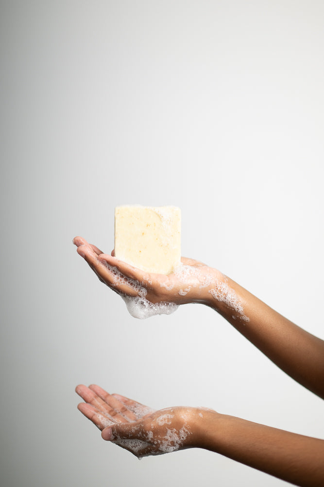Hand holding a bar of Aura-Virdys  soap with soapy water on a gray background