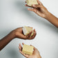 Three hands holding bars of Aura-Virdys soap against a light gray background